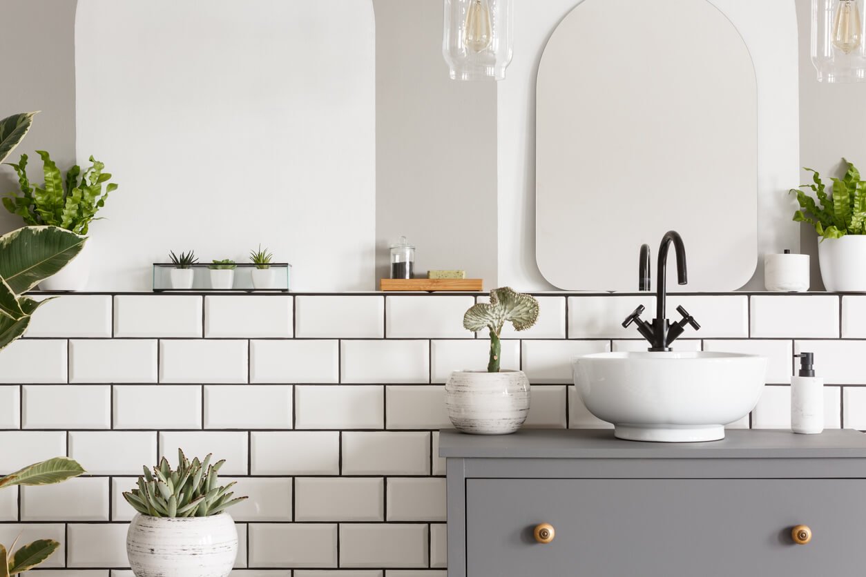 Real photo of a white sink on a grey cupboard in a bathroom interior with tiles, mirror and plants